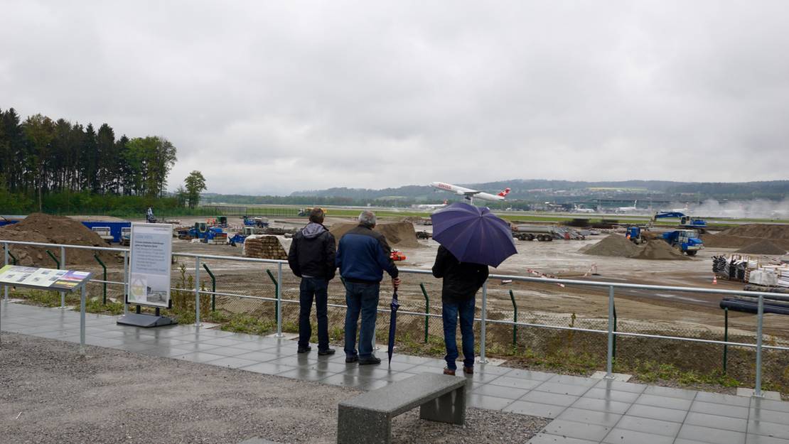 Flugzeugfans mit Schirmen beobachten ein startendes Flugzeug.